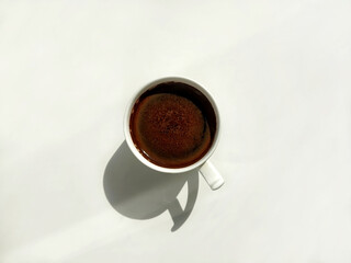 White cup of coffee on a white background with hard shadow