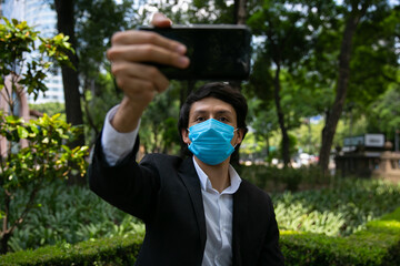 Fototapeta na wymiar Stock photo of men using mobile phone in the street. He is wearing a protective mask for the prevention of a virus. Coronavirus concept