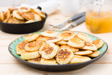 Trend breakfast. Dutch mini pancakes on a plate and a frying pan with them on a wooden table. Close-up