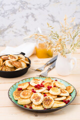 Trend breakfast. Dutch mini pancakes with red currants on a plate and a pan with them on a wooden table. Vertical