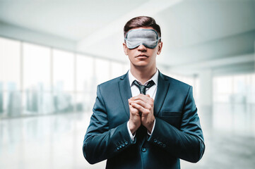 Portrait of a man in a business suit. He is praying while standing in the office. He has a sleep...
