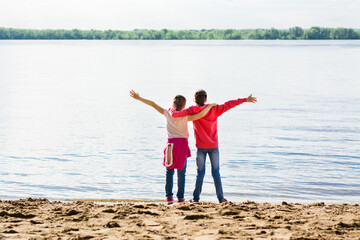 Local travel. Two girls hug on the river bank in the sand with arms outstretched. Summer tourism