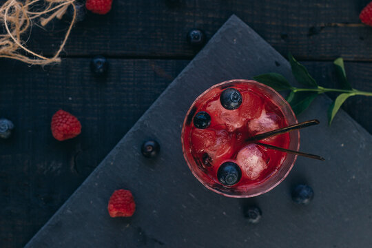 Fruity cocktail drink decorated with frozen or fresh raspberry, strawberry, rosemary, ice and soda. zenith view