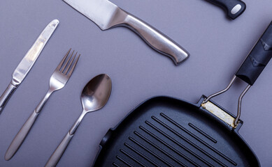 Metal knives with black on a grey table, grill pan, towel. Flat lay, layout with copy space.