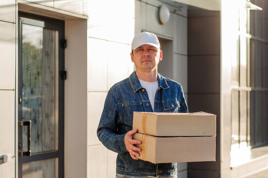 male courier in the blue costume and a cap taking out mail carton boxes from the white van on the sunny day in the street. Outdoor.