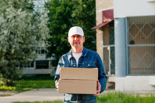 male courier in the blue costume and a cap taking out mail carton boxes from the white van on the sunny day in the street. Outdoor.
