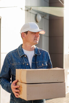 male courier in the blue costume and a cap taking out mail carton boxes from the white van on the sunny day in the street. Outdoor.