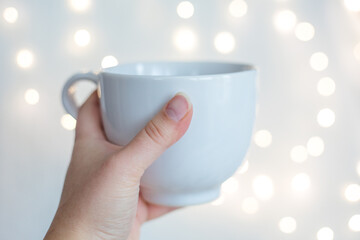 Hand with a white cup and lights in the backround