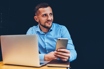 Skilled male freelancer synchronizing mobile phone files with netbook while doing remote job in...