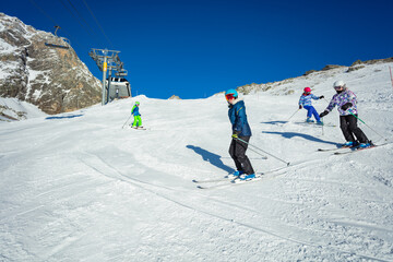 Group of kids ski downhill on Alpine slope in school formation together one after another