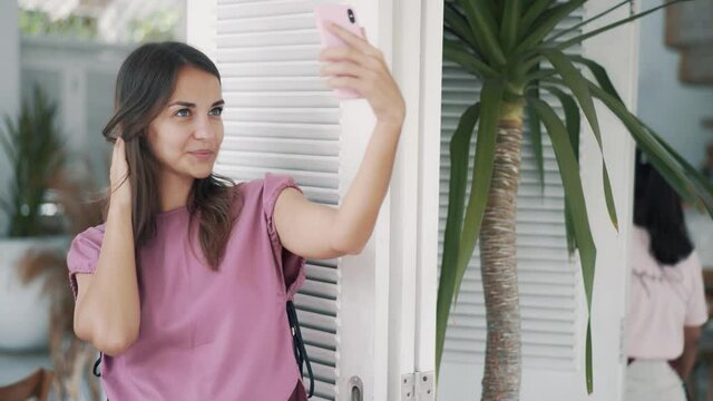 Portrait of woman in outdoor cafe, takes selfie on phone, shows peace gesture