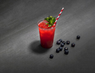a glass of red lemonade with a straw on a grey background