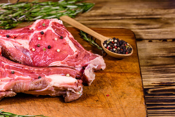 Raw ribeye steak, wooden spoon with spices and rosemary on a cutting board