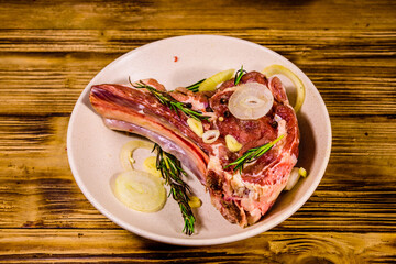 Raw ribeye steak, spices, rosemary, onion and garlic in a ceramic plate on wooden table