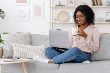 Leisure Concept. Young woman relaxing at home on the couch, having coffee and using laptop computer, copyspace
