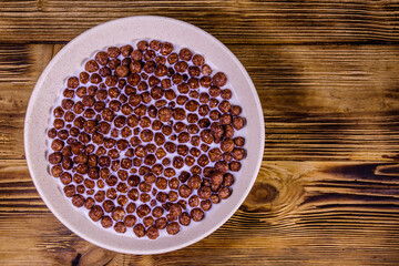 Ceramic plate with chocolate cereal balls in milk on wooden table. Top view