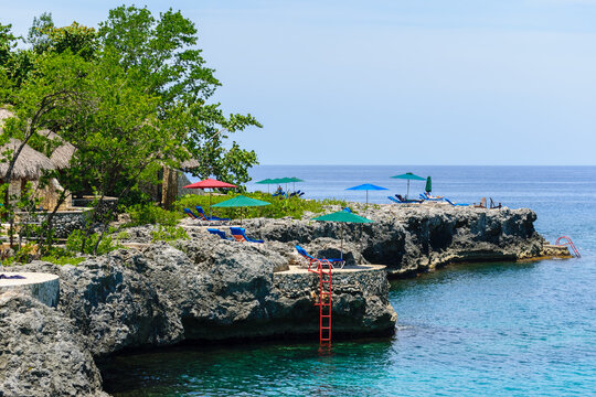 A unique location/ setting on the cliffs of Negril in Westmoreland, Jamacia. Famous vacation spot with seaside scenic views on the island coast. Thatch roof huts/ cottages, outdoor lounge chairs.