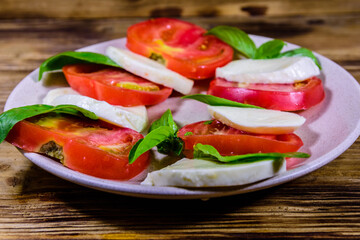 Plate with caprese salad (italian salad with cherry tomatoes, mozzarella cheese and basil leaves) on wooden table