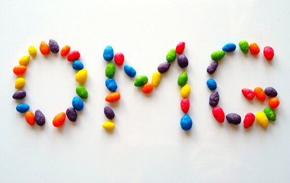 The inscription OMG, inlaid with multicolored dragees on a light, shiny surface.