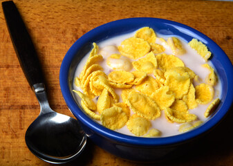 cornflakes  with yogurt in blue bowl on wooden table 