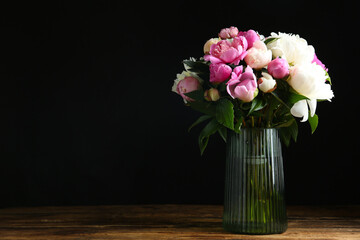 Bouquet of beautiful peonies in vase on wooden table against black background. Space for text