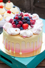 Pink cake with melted chocolate, strawberry, blueberry and cherry and cupcakes with whipped cream and fresh berries.