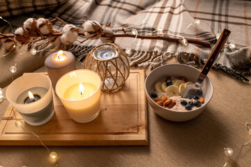 Close-up of fruit porridge and burning candles on tray place on bed with plaid