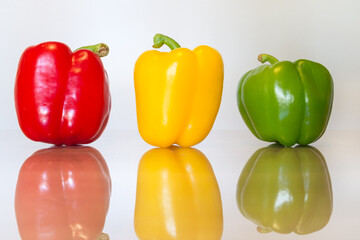 Three red, green and yellow bell peppers on a white reflective surface