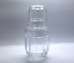 Colorless glass moringa with cup that also serves as a lid for the piece, a type of narrow vase, without spout, cylindrical and with sculpted details