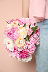 Woman with bouquet of beautiful peonies on beige background, closeup