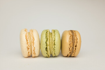 A row of three pastel coloured macarons indoors against a soft neutral background.