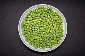Top view of a plate with fresh Green pea isolated on black background. Pisum sativum