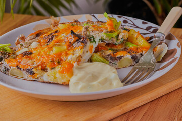 Frittata with potato and vegetables and herbs,sliced resting on a plate with some mayonnaise.