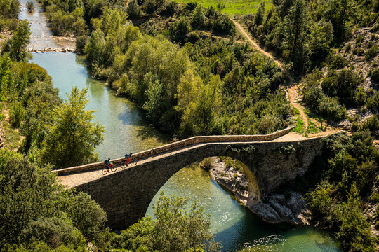 RODELLAR, HUESCA, SPAIN. Two mountain bikers ride across a narrow roman bridge over the River Alcanadre in the Sierra de Guara region. Photo: Victor Lucas