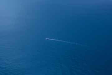A lone boat in the endless blue sea. Top view of the sea background with the ship. The concept of summer vacation. Tourist destination. Sea tour. Pleasure boat view from above.