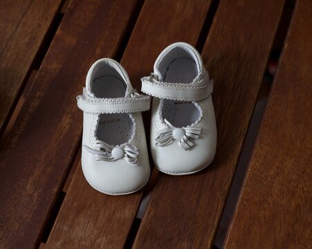 Pair of infant baby shoes with bowknot on wooden background. Stylish baby shoes color white