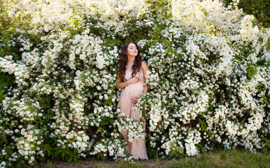 Young pregnant woman in a spring garden. Caucasian woman with long brown hairs in long romantic...