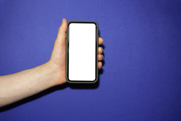 Close-up of male hand holding modern smartphone with white empty mockup on background of phantom blue color.