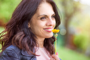 Middle-age woman in black leather jacket smiling, enjoying life, smelling flower