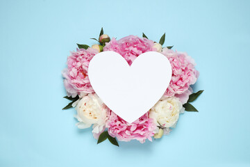Beautiful peonies and blank heart shaped card on light blue background, flat lay. Space for text