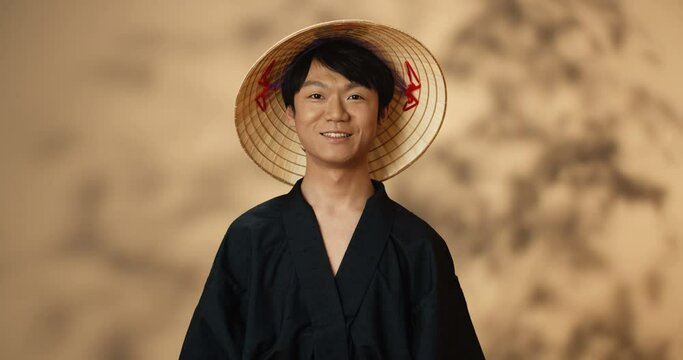 Portrait shot of young Asian handsome man in traditional clothes and conus hat smiling cheerfully and giving thumb up. Chinese good looking guy with sincere smile. Male looking cute and funny.