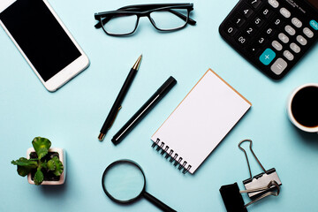 On a blue background - a pen, calculator, phone, glasses, a flower in a pot and a cup of coffee. Top view, place for an inscription, business concept