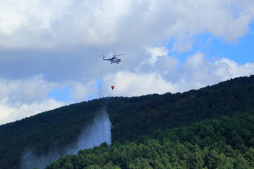 Firefighting helicopter intervenes for the fire that starts on the forest-covered mountain.