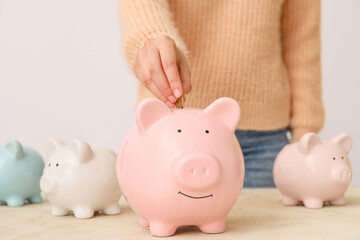 Woman putting money in piggy bank on table
