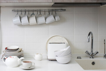White dishes: a tray, cups, plates, dishes, bowls, a toaster against the background of white kitchen trimmed with ceramics
