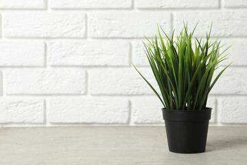 Beautiful artificial plant in flower pot on grey stone table near brick wall. Space for text
