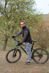 Obraz premium Sports brutal bearded guy on a modern mountain bike. Cyclist on the green hills in the spring.