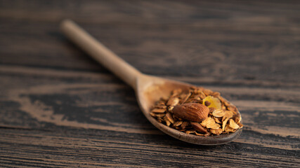 one standalone wooden spoon serving of granola with nuts. blurred wooden background. place for text. small portion