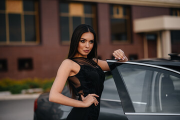 Stylish young girl stands near the car in a black dress. Business fashion and style