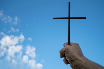 cross on blue background with clouds, supported by man's hand